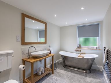 A bathroom with a freestanding bathtub a wooden vanity with a white sink and a large mirror at Foxes Den in Allerston near Thornton Dale