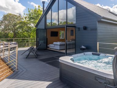 A patio with a hot tub lounge chairs sofa and glass doors leading to a living room at Foxes Den in Allerston near Thornton Dale