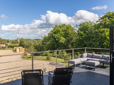 A balcony with two chairs and a grey corner sofa overlooking trees and a gravel area at Foxes Den in Allerston near Thornton Dale