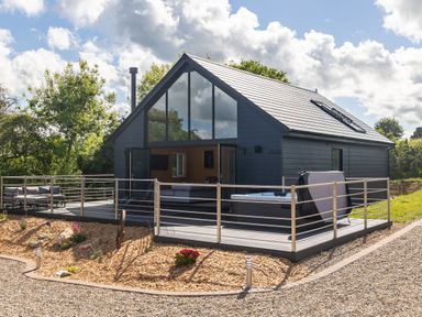 A modern house with large glass windows a wooden deck with outdoor seating and a hot tub at Foxes Den Allerston near Thornton Dale