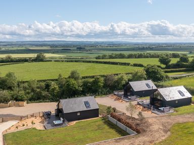 Three small black houses with decks and hot tubs surrounded by green fields at Foxes Den in Allerston near Thornton Dale