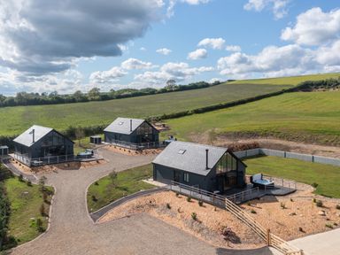 Three modern cabins with hot tubs on gravel paths near open green fields at Foxes Den in Allerston near Thornton Dale