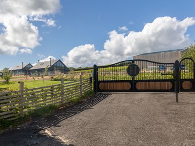 A gated entrance with a black and wooden gate and houses with large windows in the background at Foxes Den in Allerston near Thornton Dale