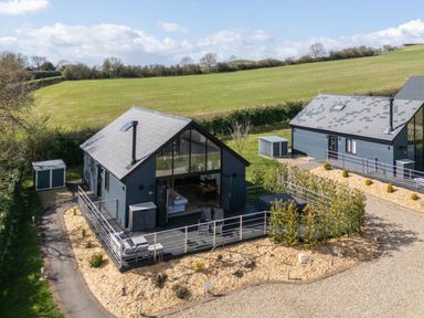 Two modern single-storey houses with dark exteriors and pitched roofs with chimneys in a rural area with grassy fields at Foxes Den in Allerston near Thornton Dale