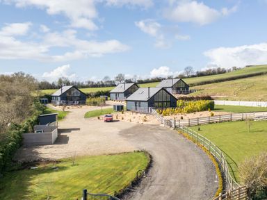 A group of four modern cabins with glass windows on a gravel road with surrounding grass and countryside at Foxes Den in Allerston near Thornton Dale