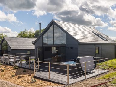 A modern cabin with large windows and a deck with seating and a hot tub at Eagles Peak in Allerton near Thornton-Le-Dale