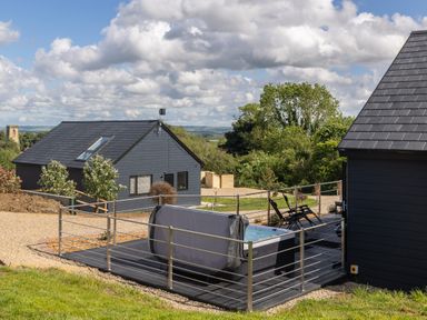 An outdoor patio area with a hot tub and chairs next to two black buildings at Eagles Peak in Allerton near Thornton-Le-Dale