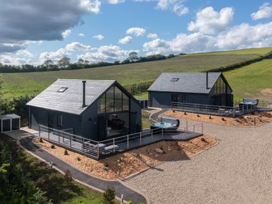 Two modern black wooden cabins with decks and hot tubs in a rural grassy landscape at Eagles Peak in Allerton near Thornton-Le-Dale