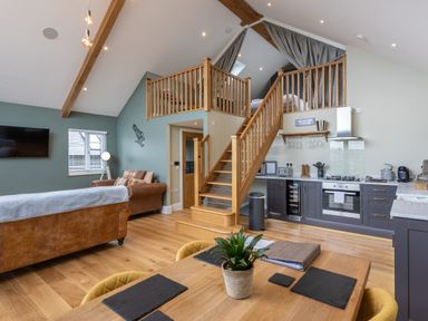 An open living area with wooden staircase leading to a loft above a kitchen with dining table in foreground at Eagles Peak in Allerton near Thornton-Le-Dale
