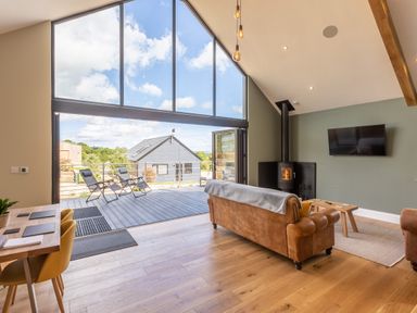 A living room with a leather sofa a wood burning stove and large glass doors opening to a deck with chairs at Eagles Peak in Allerton near Thornton-Le-Dale