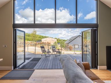 A living room with sofa facing open folding glass doors leading to a deck with two chairs at Eagles Peak in Allerton near Thornton-Le-Dale