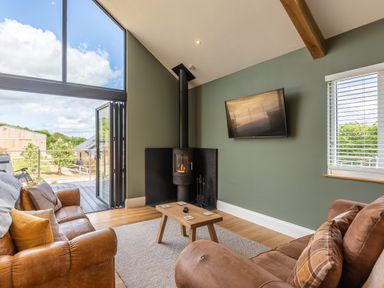 A living room with leather sofas a mounted TV a wood stove and large glass doors at Eagles Peak in Allerton near Thornton-Le-Dale