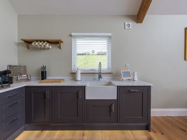 A kitchen with dark cabinets a white sink a window with blinds and a wooden shelf with mugs at Eagles Peak in Allerton near Thornton-Le-Dale
