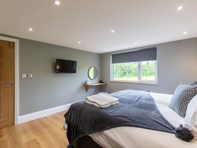 A bedroom with a bed a wall-mounted television a small shelf with a round mirror and a window at Eagles Peak in Allerton near Thornton-Le-Dale