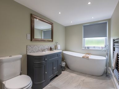 A bathroom with a toilet, sink cabinet with mirror, bathtub under a window and a towel rack at Eagles Peak in Allerton near Thornton-Le-Dale