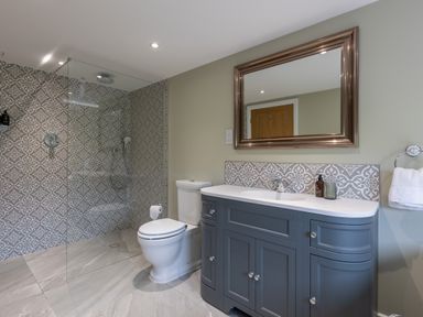 A bathroom with a toilet a shower area with patterned tiles and a blue vanity unit with a mirror at Eagles Peak in Allerton near Thornton-Le-Dale