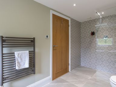 A bathroom with a wooden door a towel rail with a white towel and a shower area with patterned tiles at Eagles Peak in Allerton near Thornton-Le-Dale