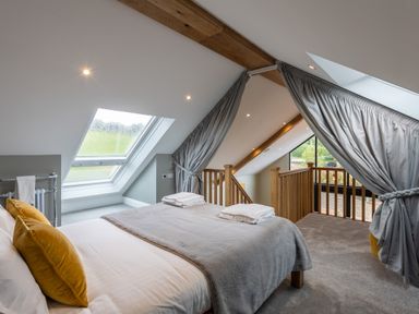 A bedroom with bed pillows a blanket skylight windows and a wooden staircase behind curtains at Eagles Peak in Allerton near Thornton-Le-Dale