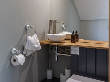 A small bathroom with a wooden countertop sink mirror hand towel soap dispensers toilet paper rolls and brush at Eagles Peak in Allerton near Thornton-Le-Dale