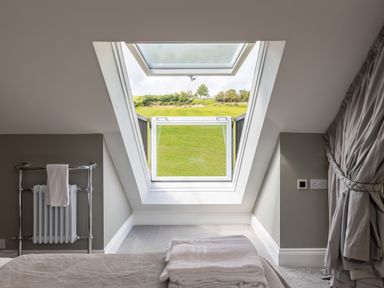 A bedroom with a slanted ceiling window showing green grass outside and towels on the bed at Eagles Peak in Allerton near Thornton-Le-Dale