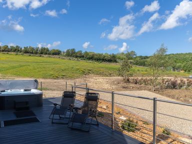 An outdoor deck with two reclining chairs and a hot tub overlooking a grassy field and trees at Eagles Peak in Allerton near Thornton-Le-Dale