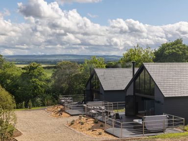 Two modern cabins with large glass windows and deck areas in a countryside setting with trees and hills at Eagles Peak in Allerton near Thornton-Le-Dale