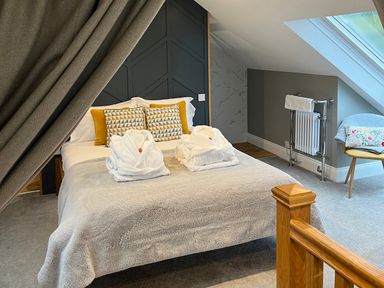 A bedroom with a double bed with pillows and robes near a window and a chair at Eagles Peak in Allerton near Thornton-Le-Dale
