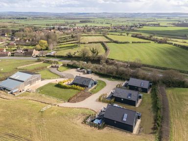 A rural area with four black houses a large barn and green fields at Eagles Peak in Allerton near Thornton-Le-Dale