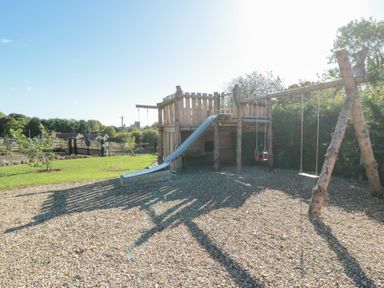 A playhouse with a slide and swings in an outdoor play area at Eagles Peak Allerton near Thornton-Le-Dale