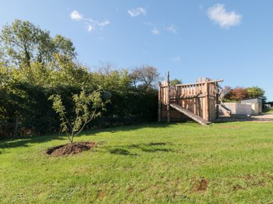 An outdoor playground with a wooden playhouse and tree at Eagles Peak, Allerton near Thornton-Le-Dale