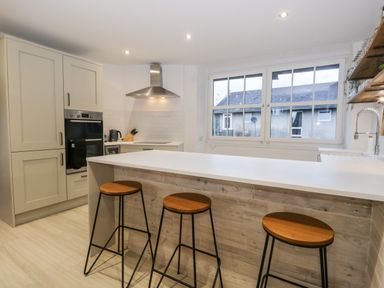 A kitchen with three bar stools at a counter and large window at Dixon Court in Ambleside