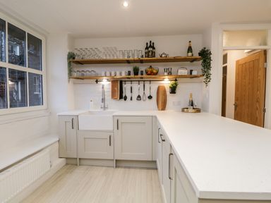 A kitchen with white countertops open wooden shelves hanging utensils and a window at Dixon Court in Ambleside