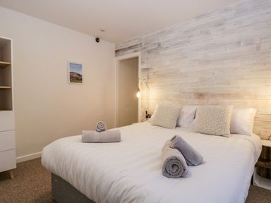 A bedroom with a large bed pillows rolled towels wooden accent wall and a small framed picture at Dixon Court in Ambleside