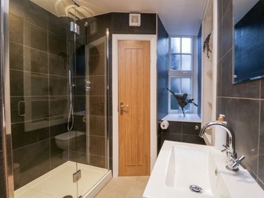 A bathroom with a glass shower enclosure wooden door sink and window with a vase at Dixon Court in Ambleside