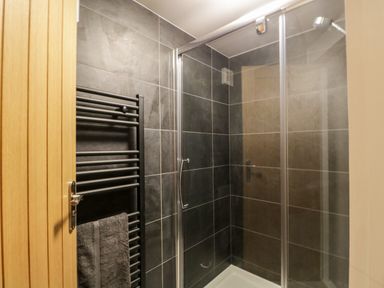 A shower area with glass door dark tile walls black heated towel rail and wooden door at Dixon Court Ambleside