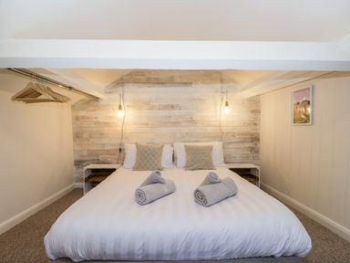 A bedroom with a double bed, two rolled towels, hanging lights, and an open closet at Dixon Court in Ambleside