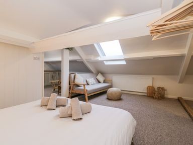 A loft bedroom with a bed and rolled towels a sofa with cushions and a small table under a skylight at Dixon Court in Ambleside