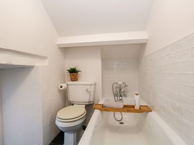 A bathroom with a toilet a bathtub with a wooden bath tray and tiled walls at Dixon Court in Ambleside