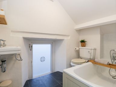A bathroom with a sink toilet and bathtub with a wooden bath tray and small window at Dixon Court in Ambleside