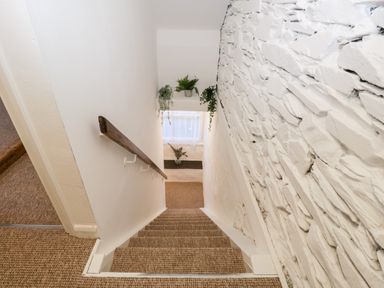 A staircase with carpeted steps and a wooden handrail next to a white stone wall at Dixon Court in Ambleside