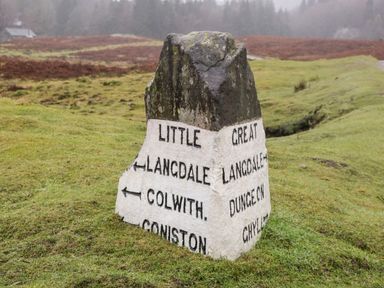 A stone direction marker on grass with text pointing to Little Langdale and Colwith and Great Langdale Dungeon Ghylf at Dixon Court Ambleside