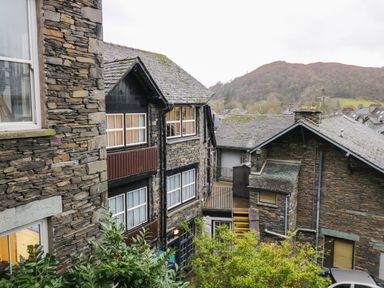 Stone buildings with multiple windows and rooftops with a background of trees and hills at Dixon Court in Ambleside