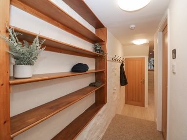 A hallway with wooden shelves holding plants and a hat and a coat rack with a coat at Dixon Court in Ambleside
