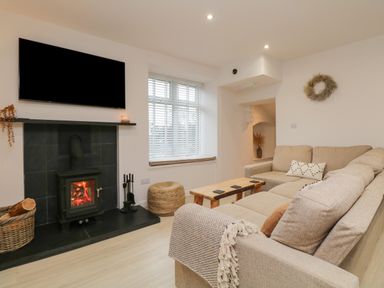A living room with a fireplace a TV a beige sectional sofa and a wooden coffee table at Dixon Court in Ambleside