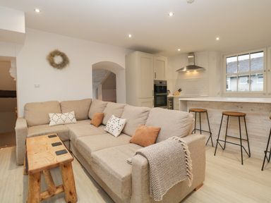 A beige sectional sofa with pillows and a throw blanket next to a wooden bench and kitchen with bar stools at Dixon Court in Ambleside