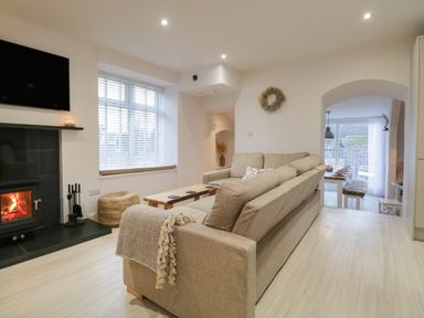 A living room with a beige sofa a wooden coffee table a fireplace and a dining area visible through an arch at Dixon Court in Ambleside