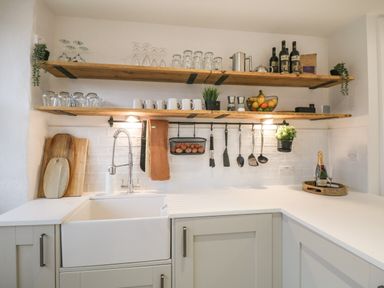 A kitchen area with wooden shelves holding glasses mugs and bottles above a white sink and countertop at Dixon Court in Ambleside