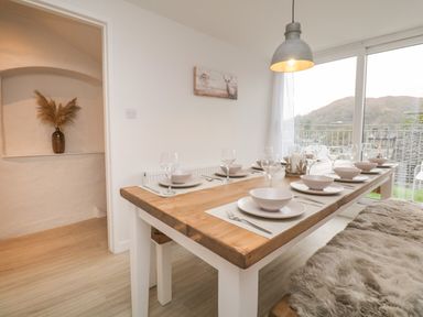 A dining room with a wooden table set with plates bowls wine glasses and cutlery next to a large window with a view of hills at Dixon Court in Ambleside