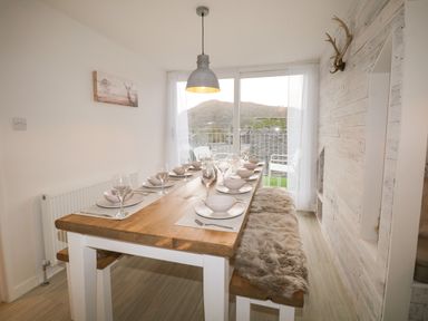 A dining area with a wooden table set with bowls and glasses beside large windows with a view at Dixon Court Ambleside