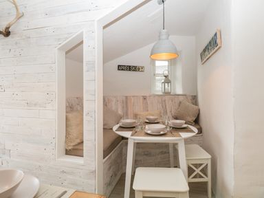 A small dining nook with a round table set for four surrounded by built-in bench seating with pillows and two stools at Dixon Court in Ambleside